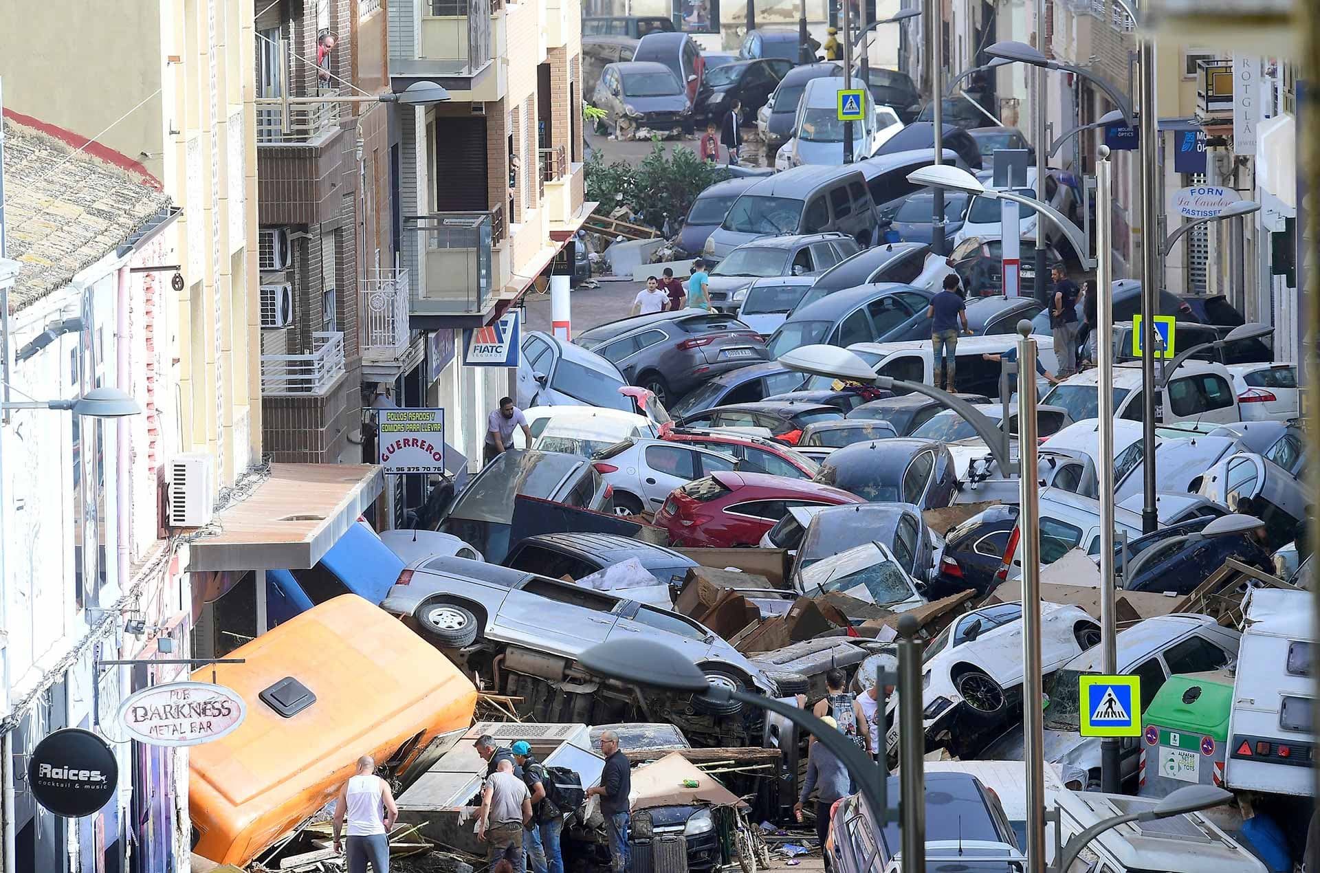 Peatones intentan caminar entre los coches amontonados en Valencia después del paso de una DANA