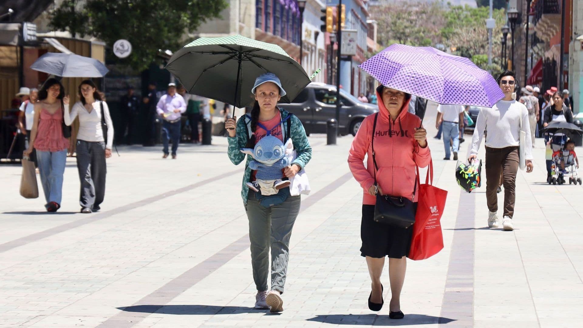 Dos mujeres caminan y usan sombrillas para protegerse del calor en Oaxaca